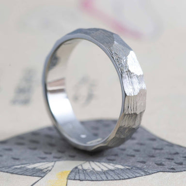 14kt white gold custom carved wedding ring with rough faceted texture, angled on paper