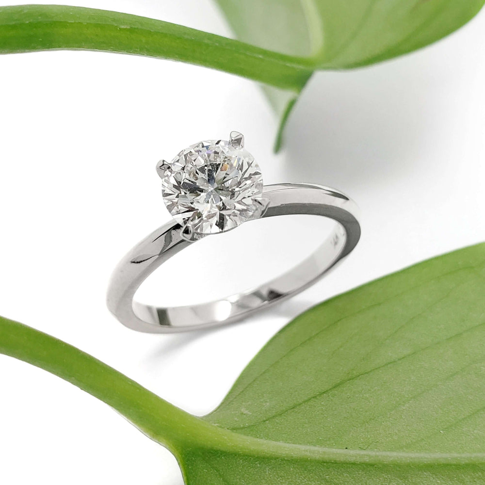 14kt white gold lab diamond engagement ring beside green leaves, angled view