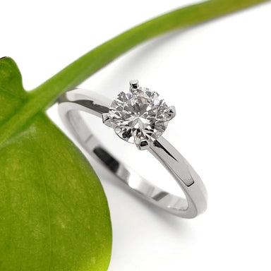 14kt white gold lab diamond solitaire ring beside a green leaf