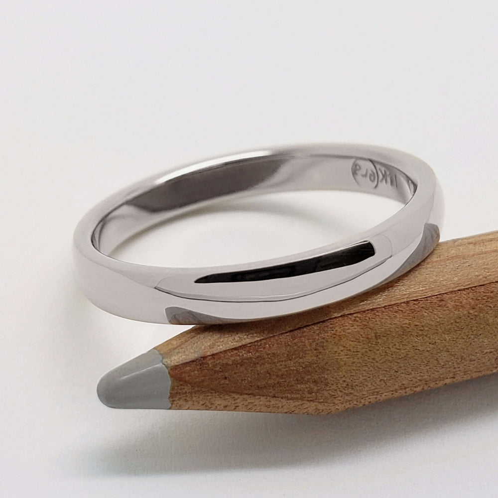 14kt white gold low dome wedding ring resting on a wooden pencil