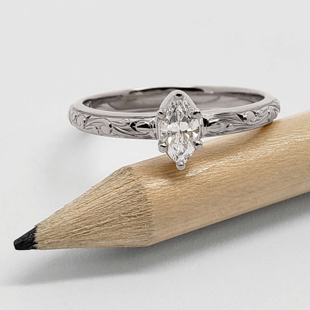 14kt white gold marquise lab diamond ring with engraved band beside a pencil