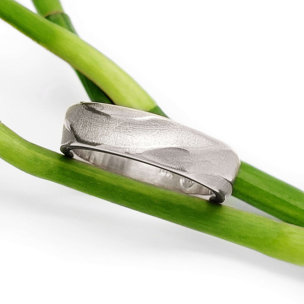 14kt white gold topography textured wedding ring resting on green stems