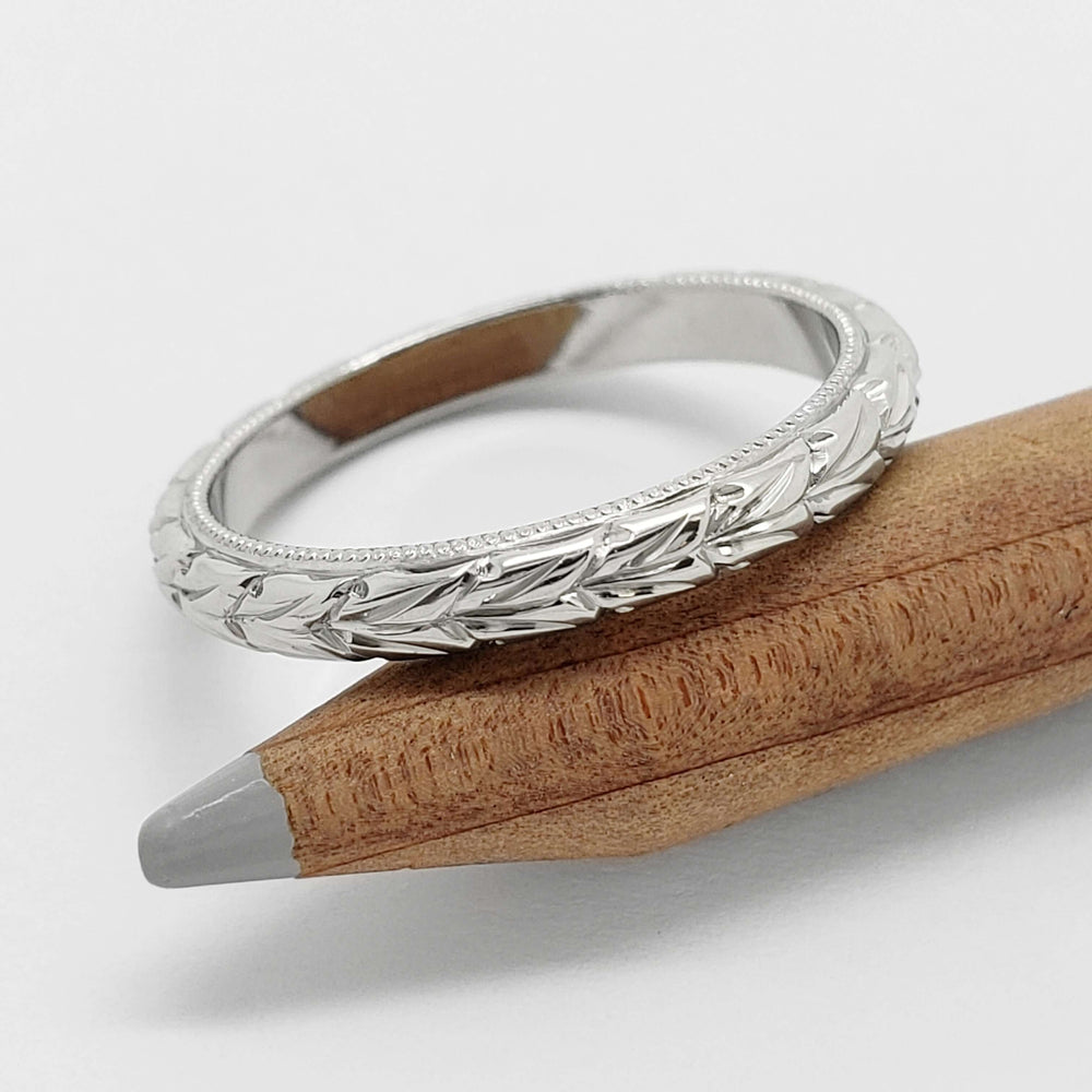 14kt white gold wheat engraved wedding ring with millgrain, resting on pencil