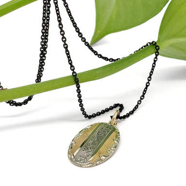Engraved 14kt yellow and white gold pendant displayed on a black chain with a green plant