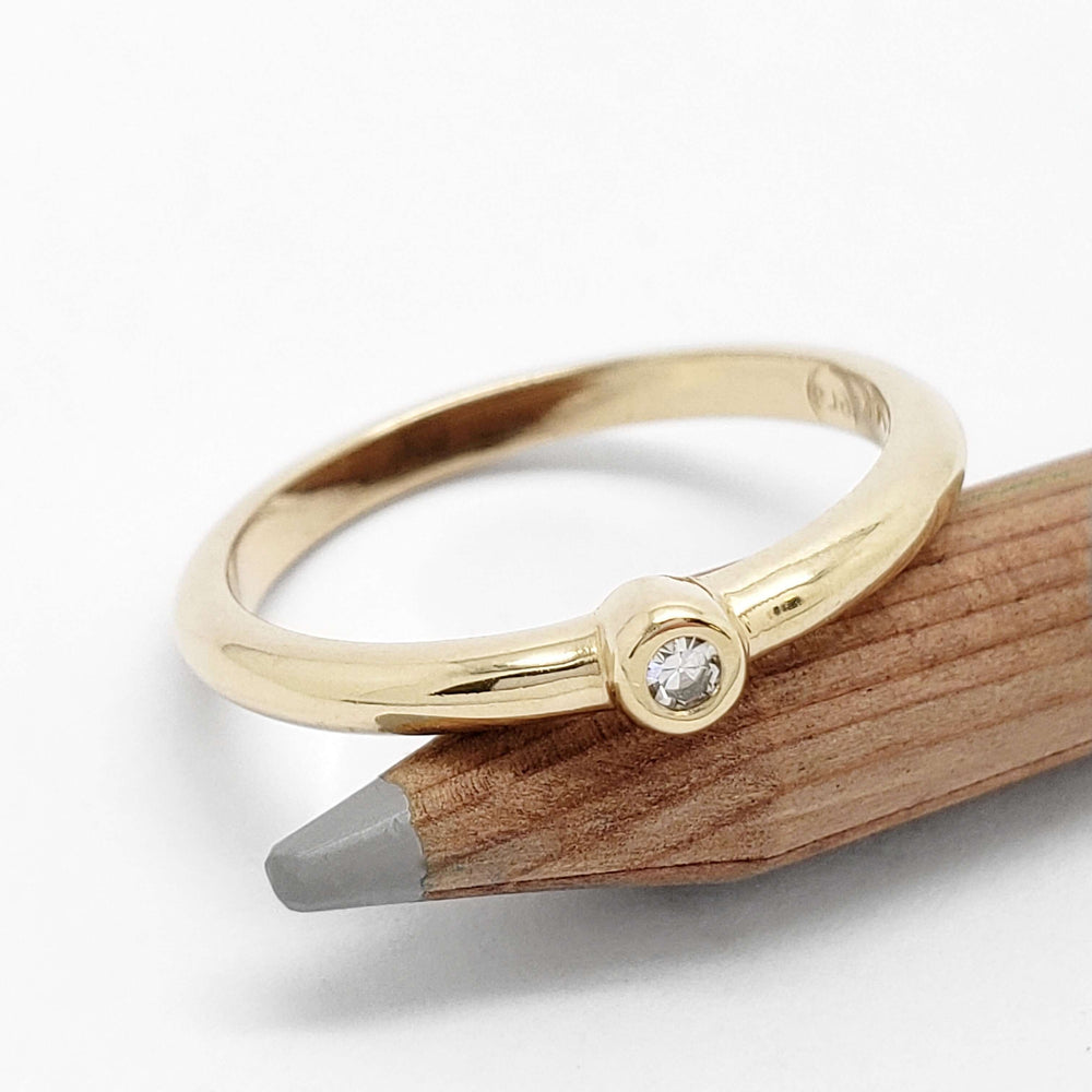 14kt yellow gold bezel set diamond ring displayed on a pencil