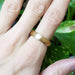 14kt yellow gold brushed wedding ring shown on hand with green foliage