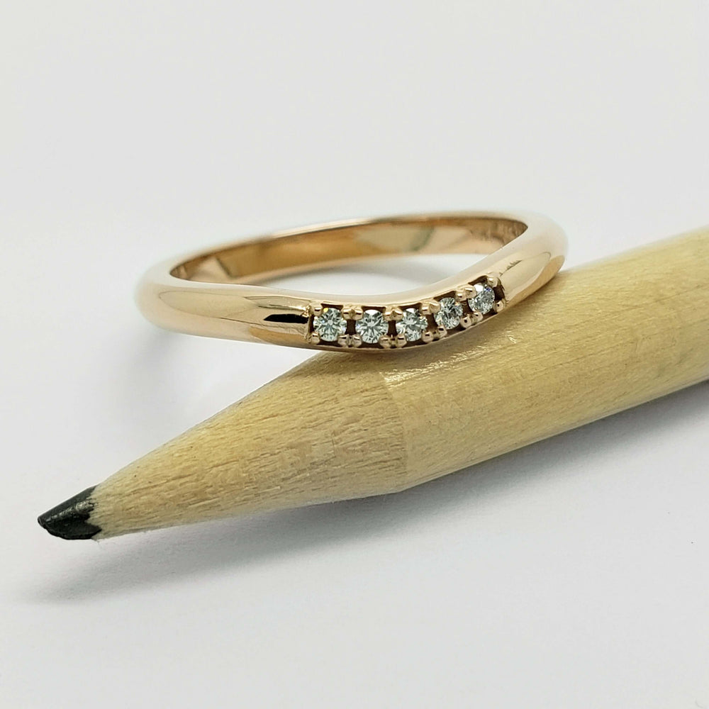 14kt yellow gold chevron diamond wedding ring resting on a pencil