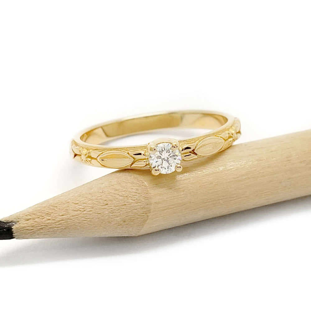 14kt yellow gold diamond engagement ring with engraved details beside a pencil