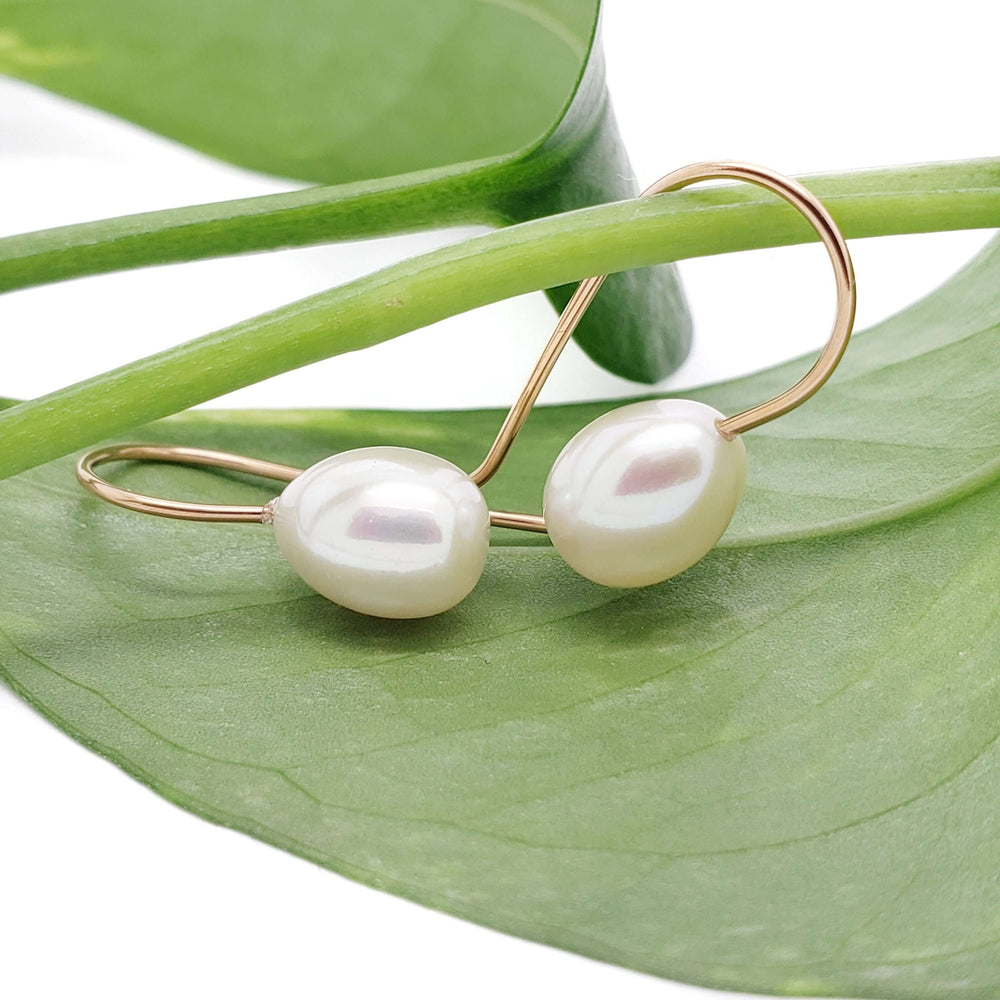 Pair of 14kt yellow gold drop earrings with freshwater pearls resting on a green leaf