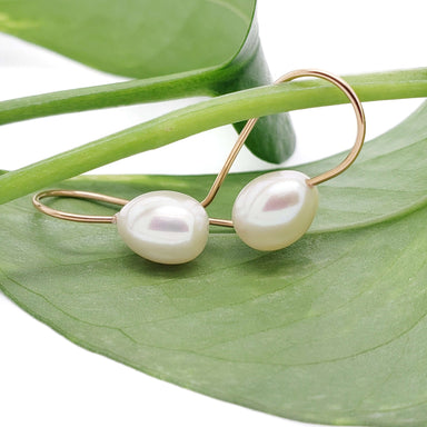 Pair of 14kt yellow gold drop earrings with freshwater pearls resting on a green leaf