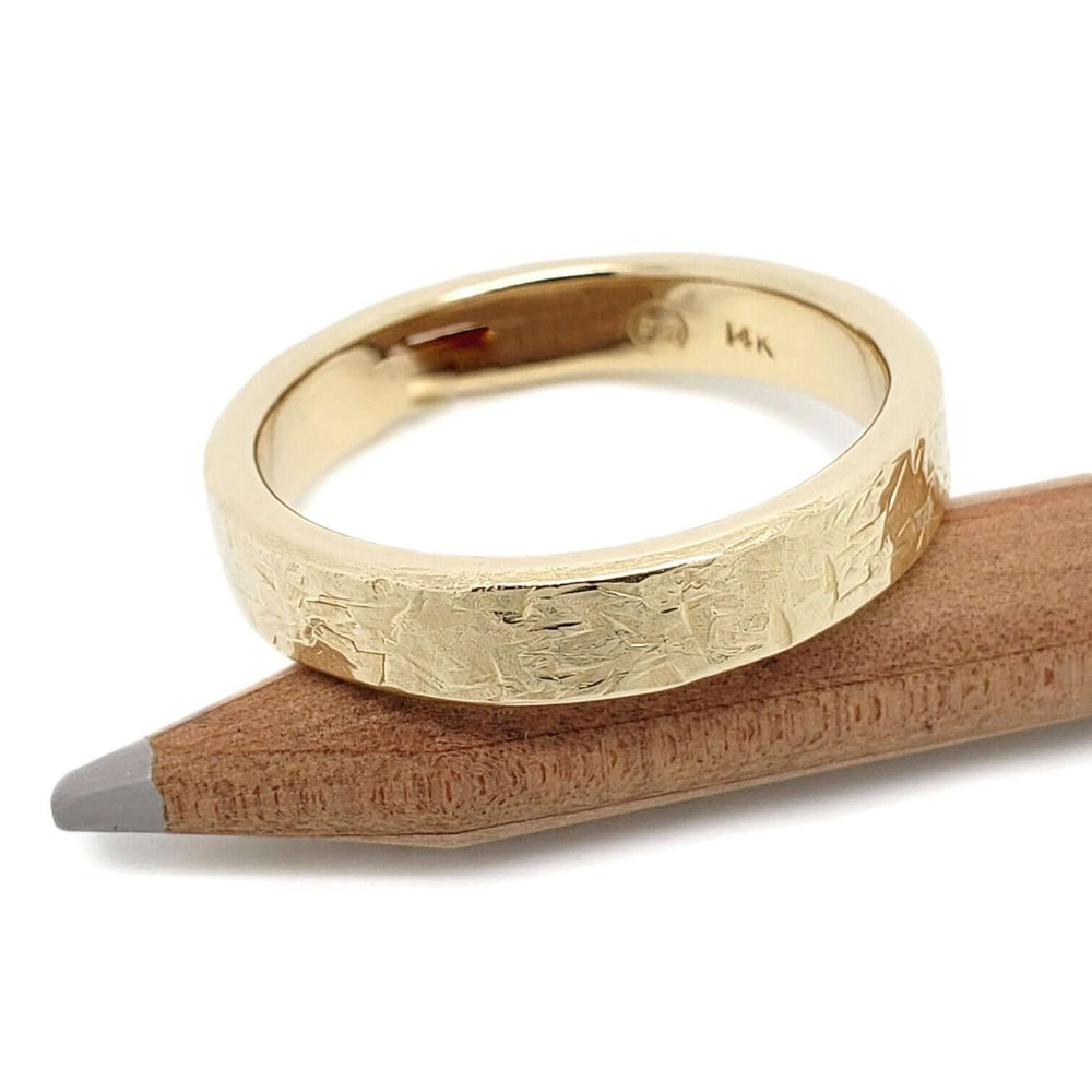 14kt yellow gold elephant skin textured wedding ring resting on a pencil