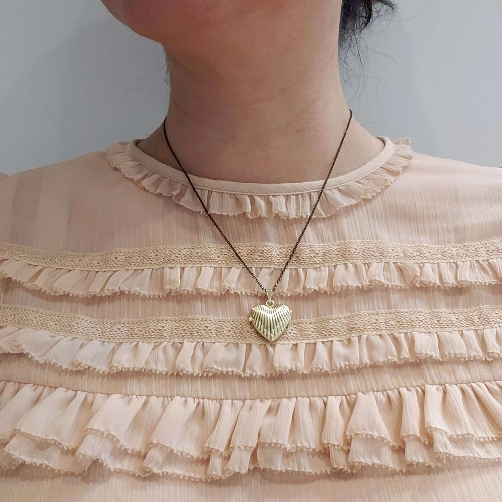 Vintage embossed gold heart locket worn on a model with a black chain