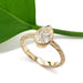 A gold ring with an engraved band and a pear-cut reclaimed diamond, styled on a white background with a green leaf prop.