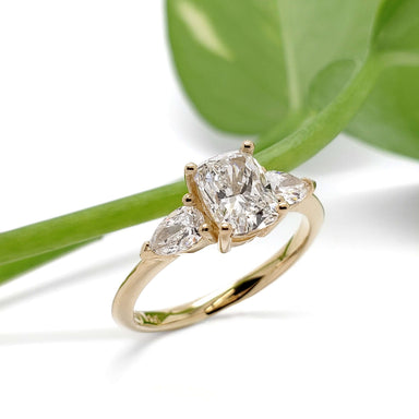 14kt yellow gold engagement ring with cushion and pear cut lab diamonds, shown with green leaf