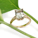 14kt yellow gold engagement ring with green sapphire and lab diamonds, shown with green leaves