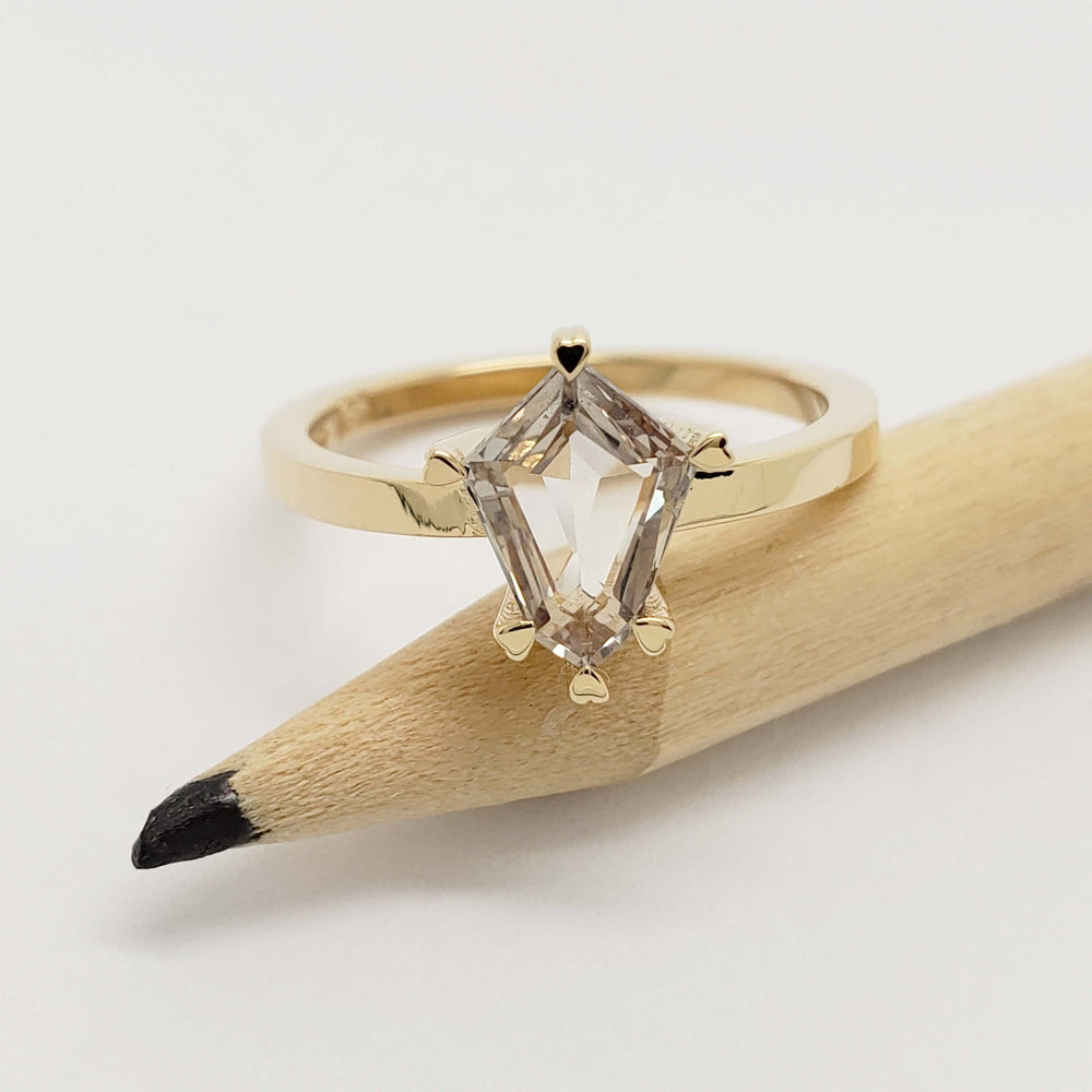 14kt yellow gold engagement ring with shield cut grey sapphire, shown on a pencil