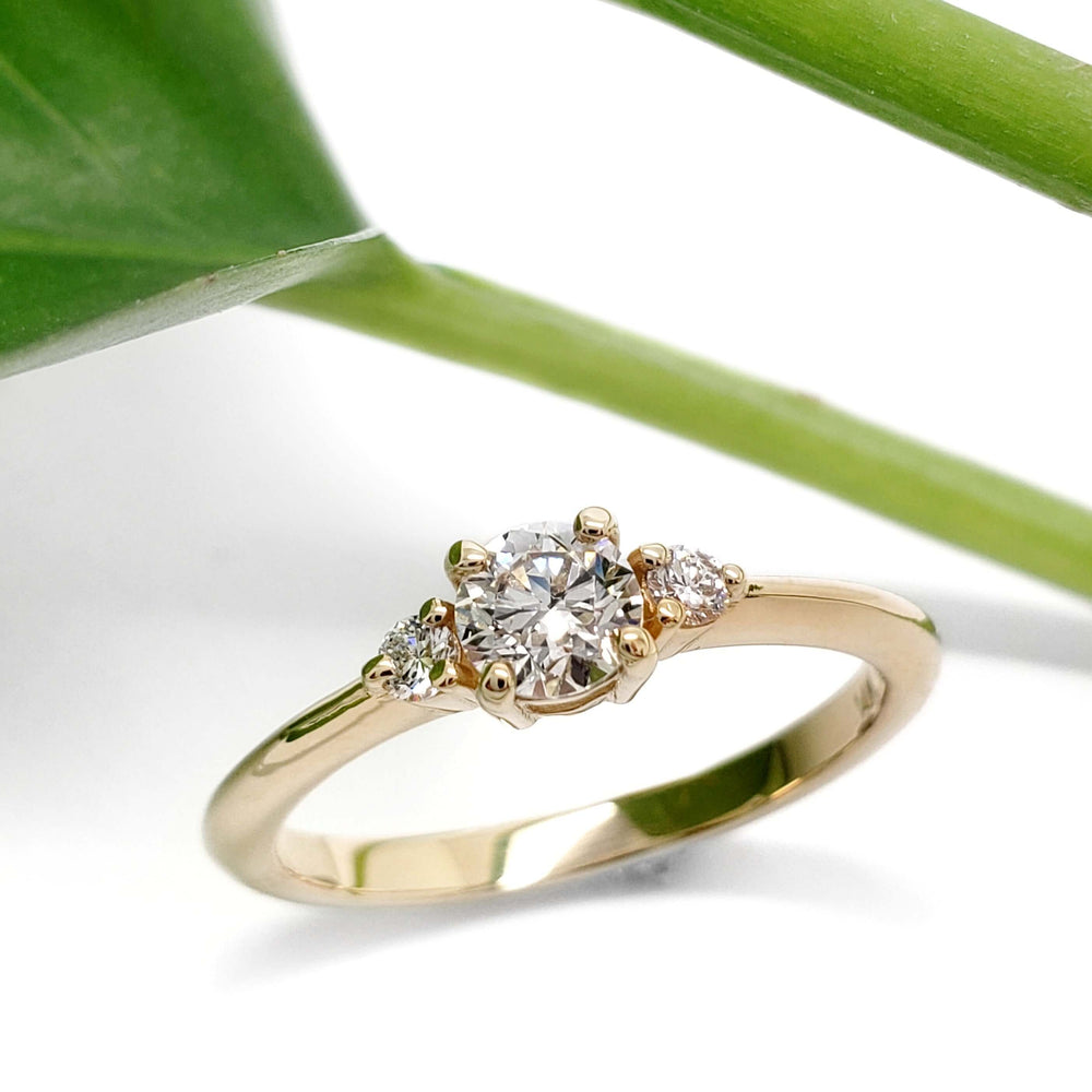 14kt yellow gold engagement ring with vintage diamond and lab-grown side stones, beside a green leaf