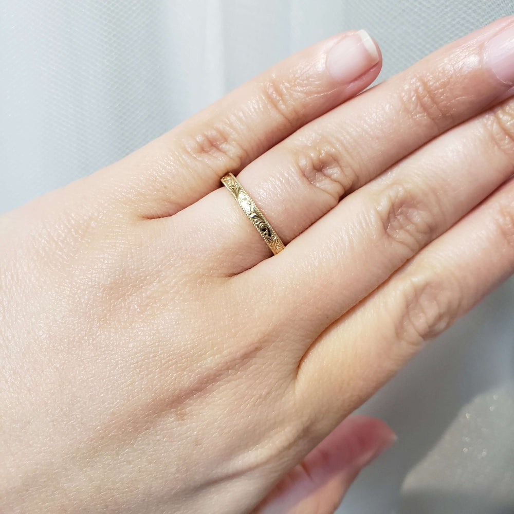 14kt yellow gold engraved wedding ring with millgrain detail shown on a hand