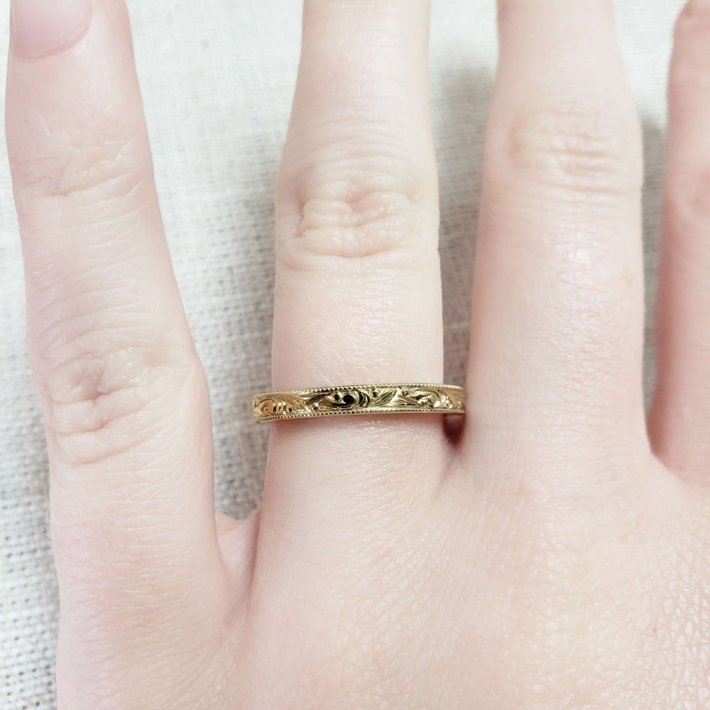 14kt yellow gold engraved wedding ring with millgrain edge shown on hand
