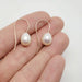 Pair of 14kt yellow gold freshwater pearl drop earrings shown on a hand