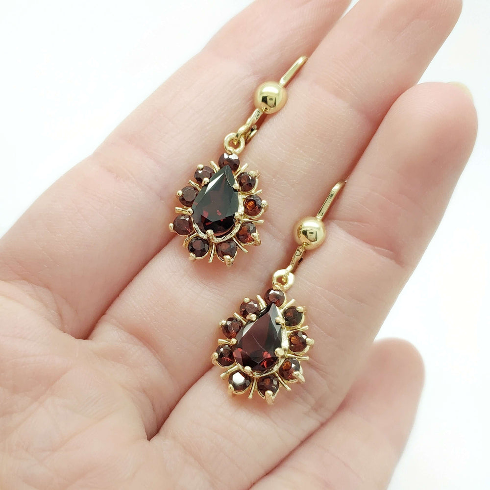 14kt yellow gold garnet dangle earrings shown resting on a hand for scale