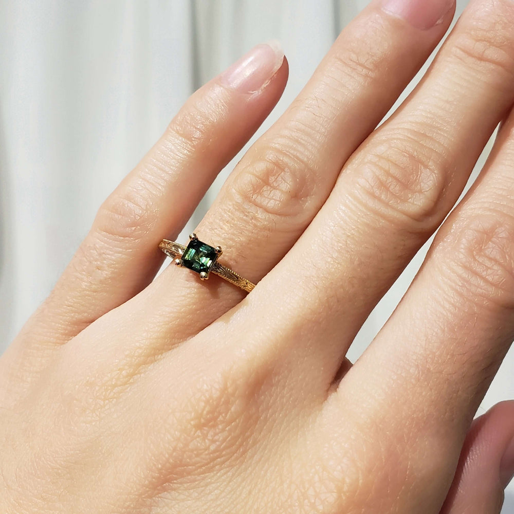 14kt yellow gold green sapphire engagement ring worn on hand, showing engraved band