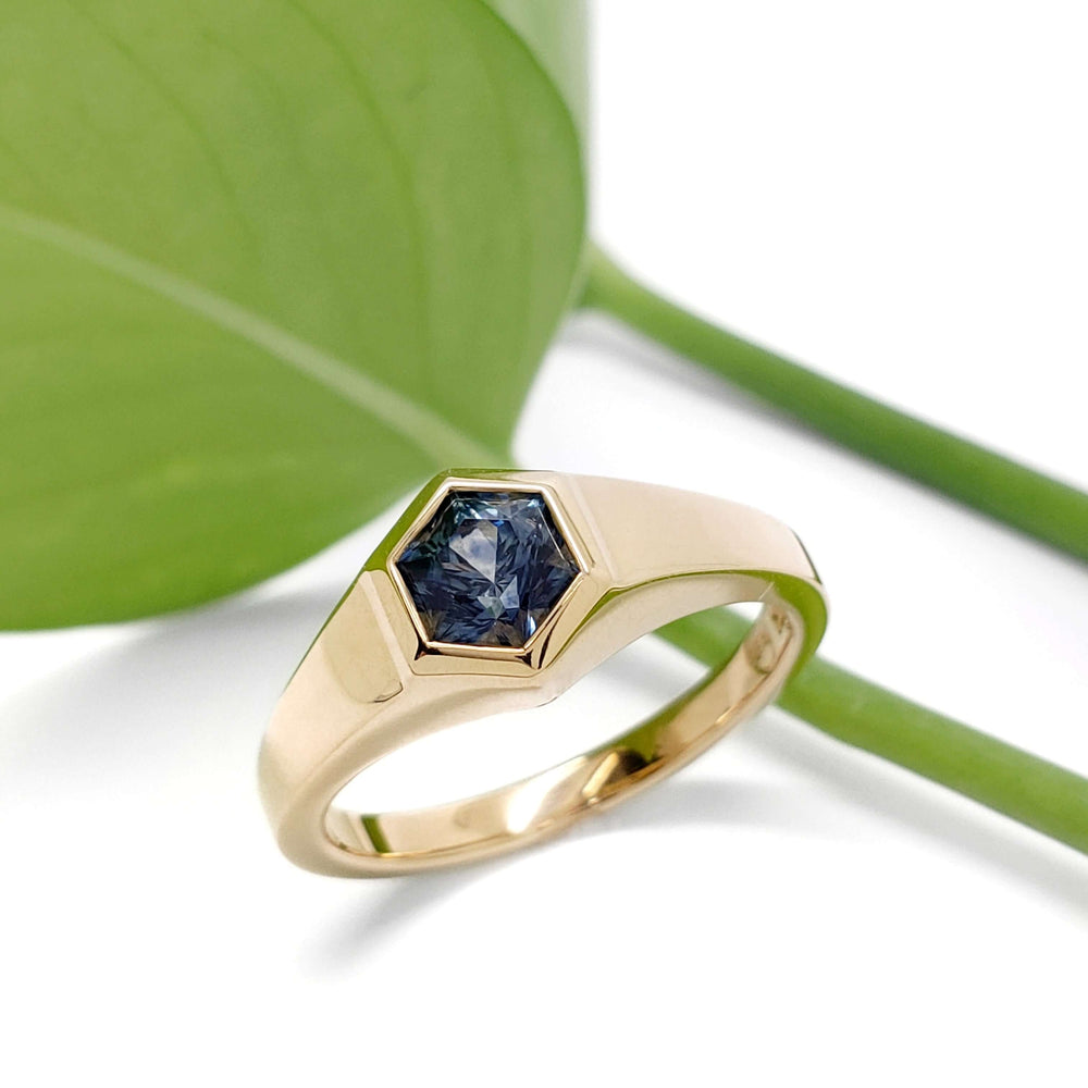 14kt yellow gold hexagon Montana sapphire ring beside a green leaf