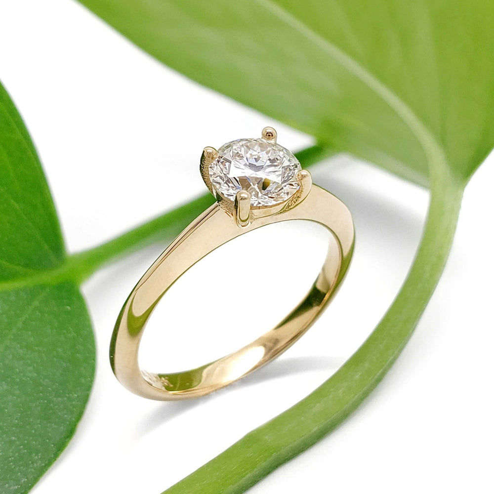 14kt yellow gold lab diamond engagement ring with solitaire setting, beside green leaves