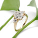 14kt yellow gold engagement ring with oval lab diamond and two round lab diamonds, shown with green leaves