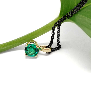 14kt yellow gold lab emerald pendant with black chain, shown with green leaf