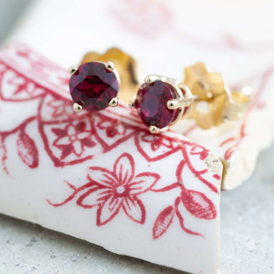 Close-up of 14kt yellow gold lab grown ruby stud earrings on patterned ceramic