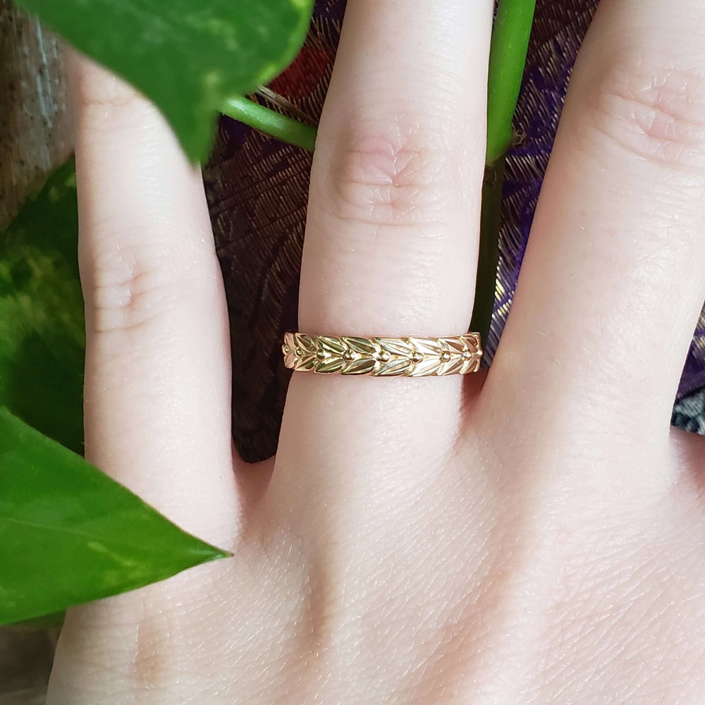 14kt yellow gold leaf engraved wedding ring shown on a finger