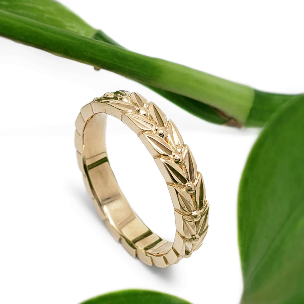 14kt yellow gold leaf engraved wedding ring with green leaves in background