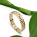 14kt yellow gold leaf engraved wedding ring with green leaves in background