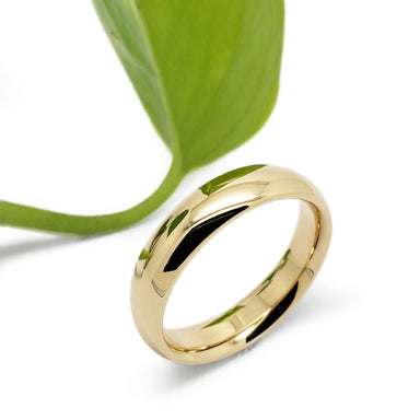 14kt yellow gold low dome wedding ring beside a green leaf