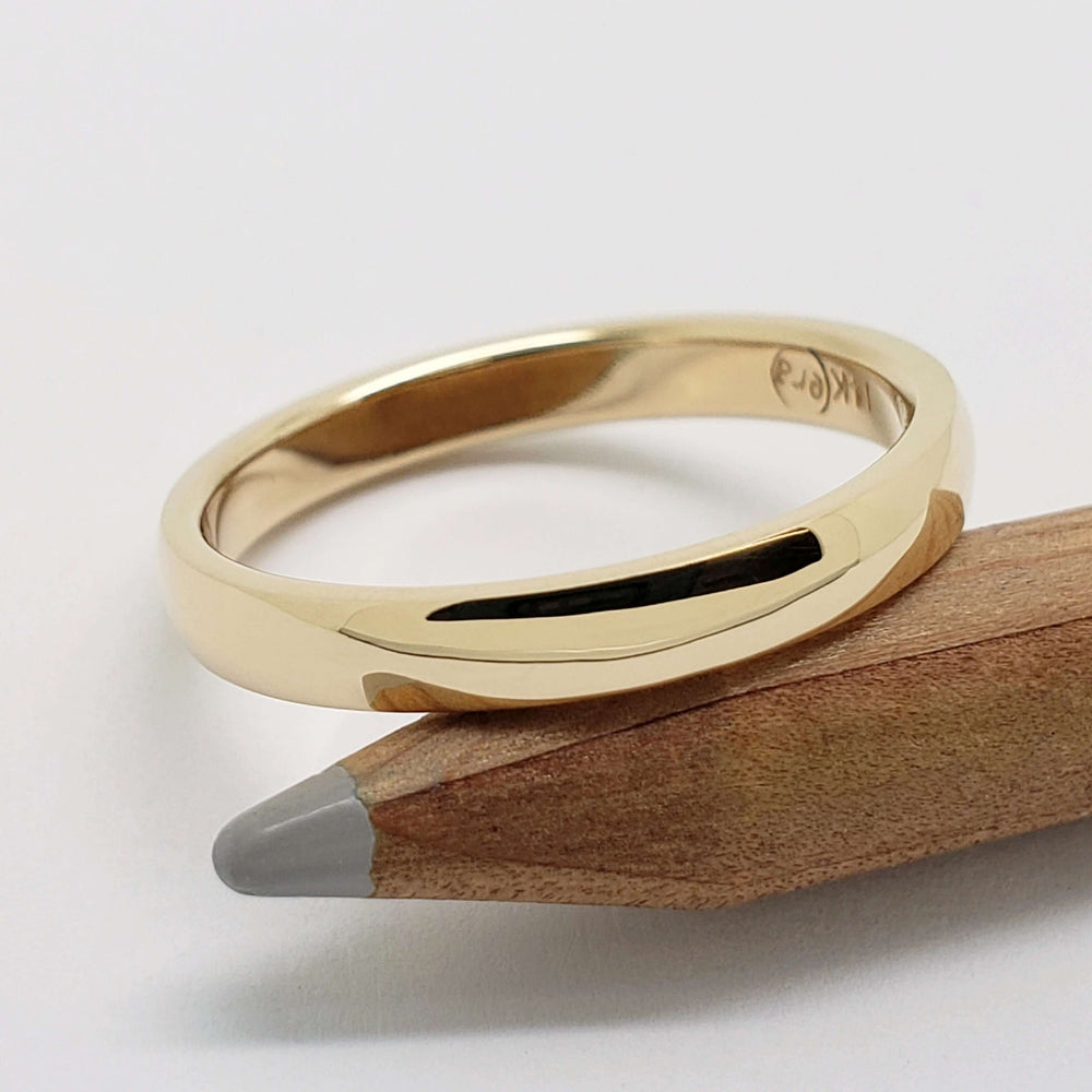 14kt yellow gold low dome wedding ring resting on a pencil