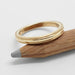 14kt yellow gold millgrain wedding ring resting on a wooden pencil