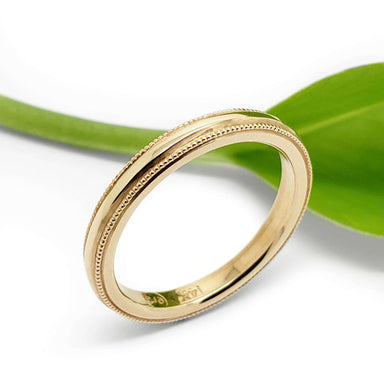 14kt yellow gold millgrain wedding ring beside a green leaf