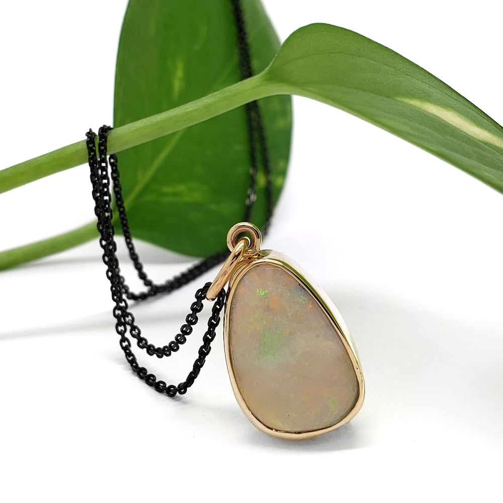 14kt yellow gold opal bezel pendant displayed with black chain and green leaf