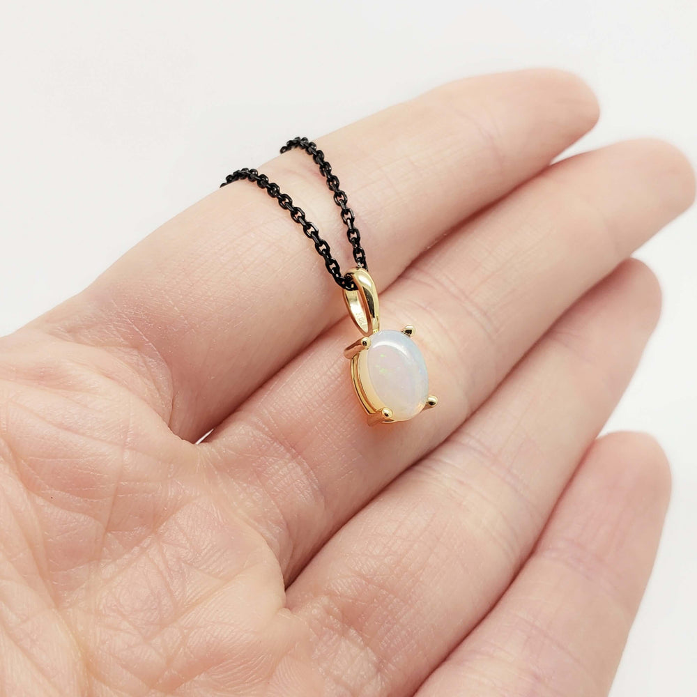 Hand holding 14kt yellow gold opal pendant with oval cabochon on black chain