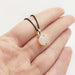 Hand holding 14kt yellow gold opal pendant with oval cabochon on black chain