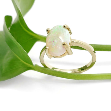 14kt yellow gold opal ring with oval cabochon white opal beside green leaves