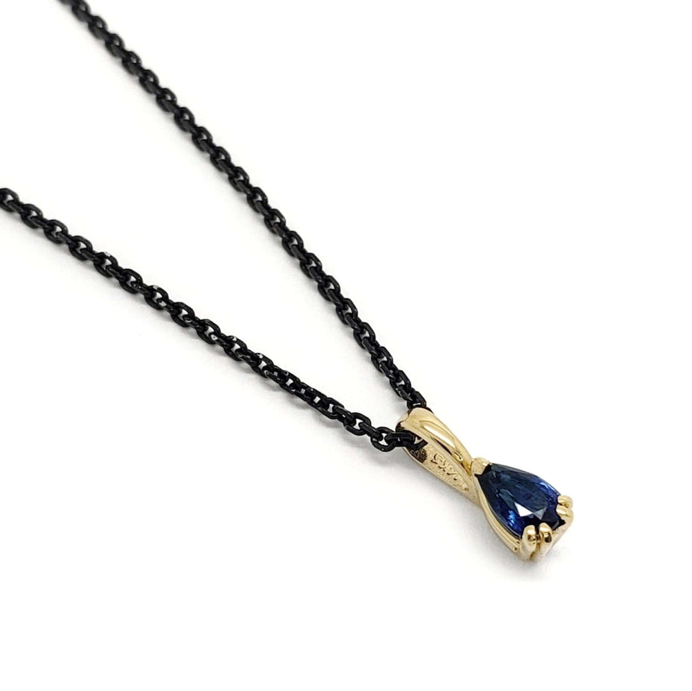 14kt yellow gold pendant with pear cut blue sapphire on black chain, angled view