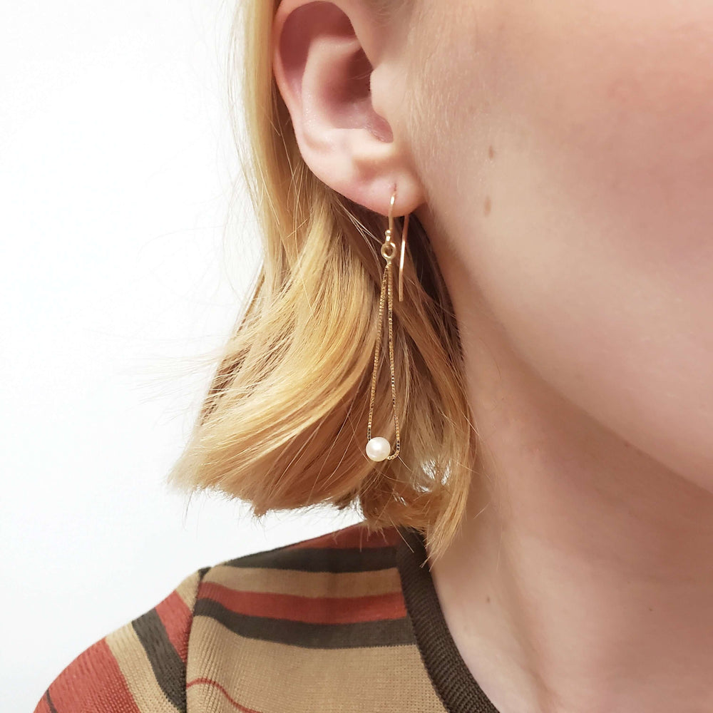 Model wearing a 14kt yellow gold teardrop earring with freshwater pearl
