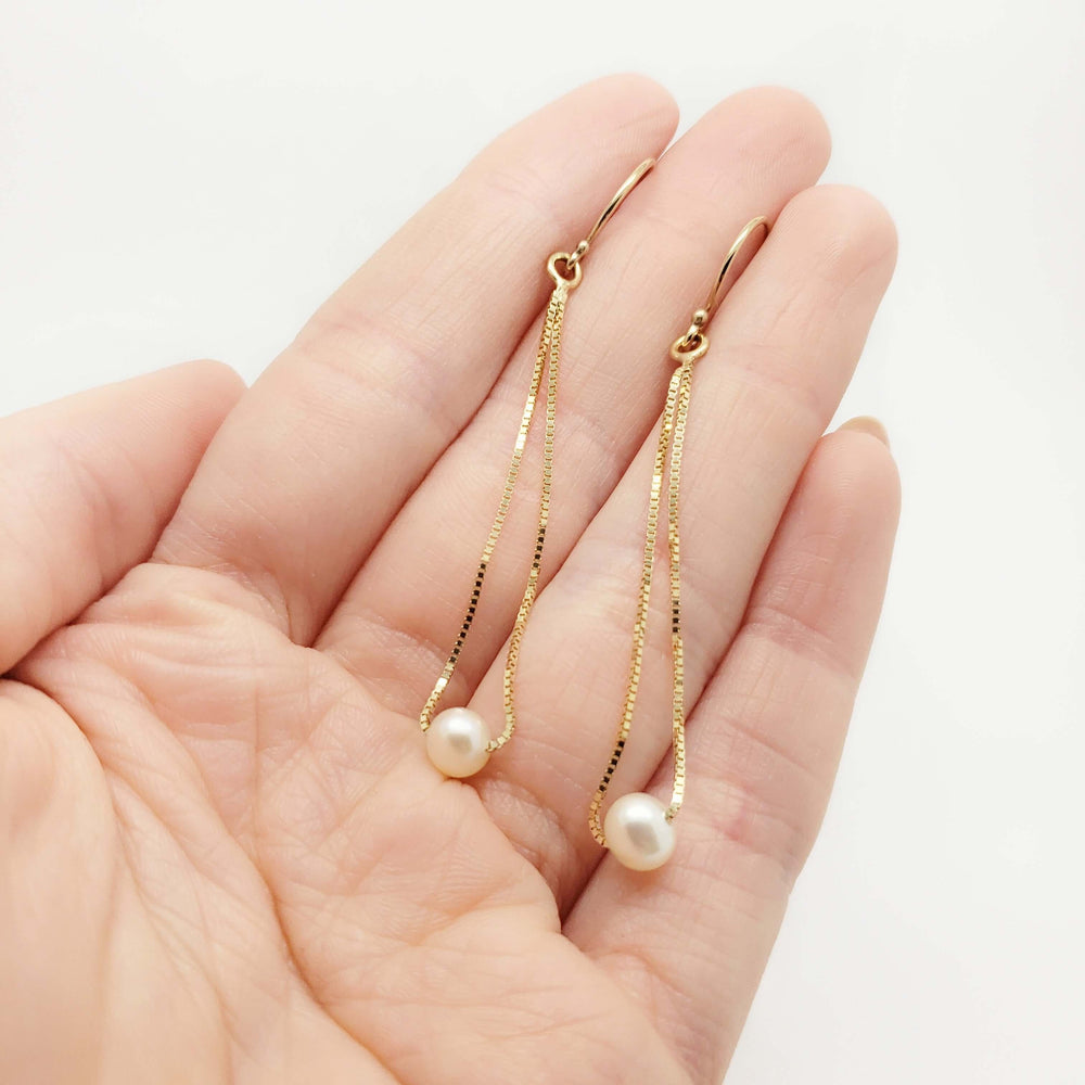Hand holding 14kt yellow gold teardrop earrings with freshwater pearls