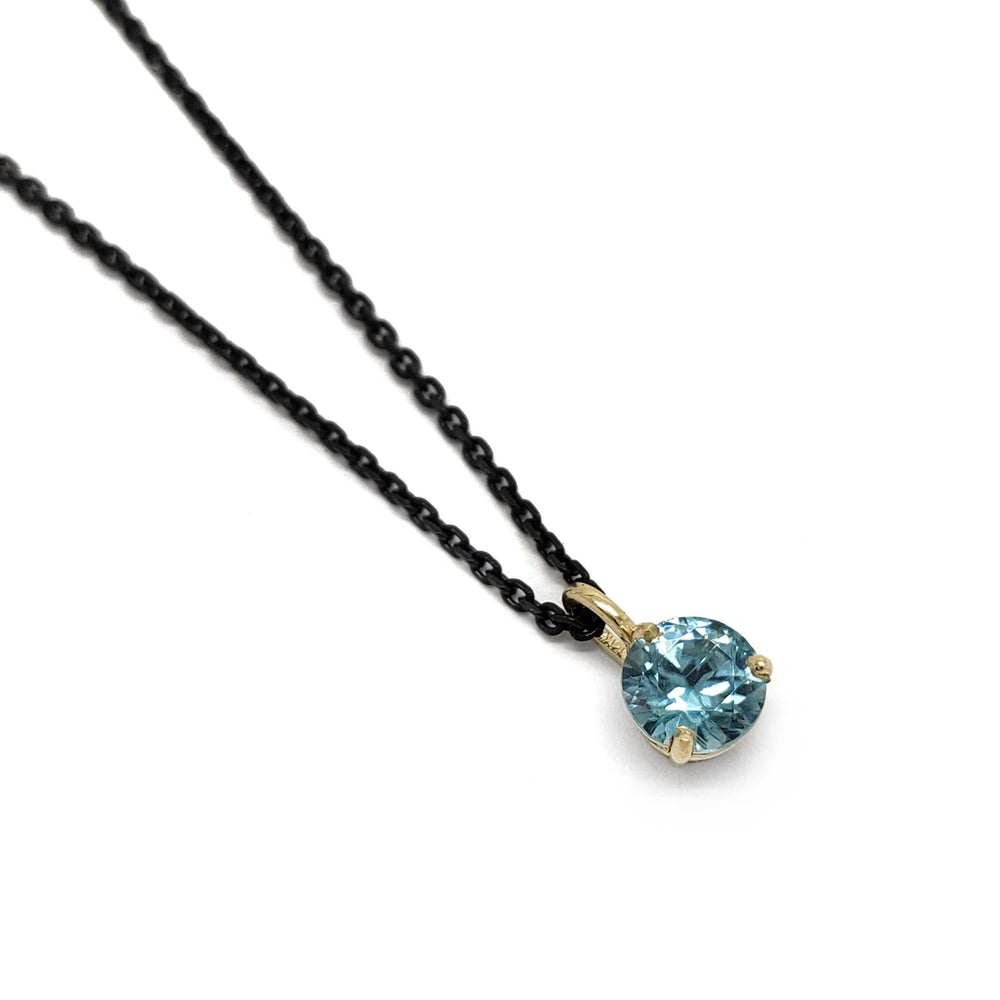 14kt yellow gold pendant with round blue zircon on a black chain, angled view