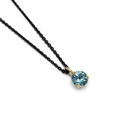 14kt yellow gold pendant with round blue zircon on a black chain, angled view