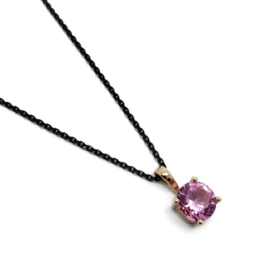 14kt yellow gold pendant with round pink spinel on black chain, studio background
