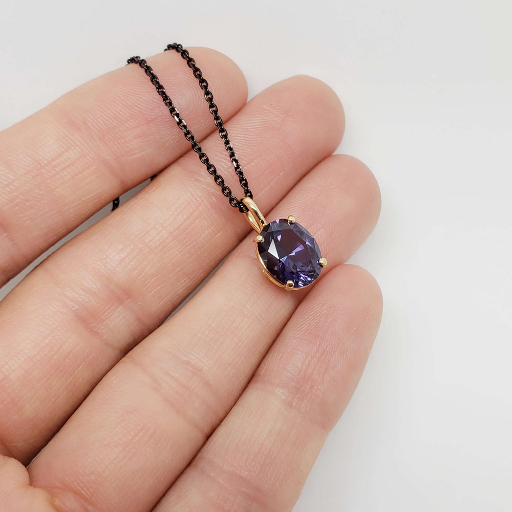 14kt yellow gold purple sapphire pendant on black chain, shown resting on fingers for scale