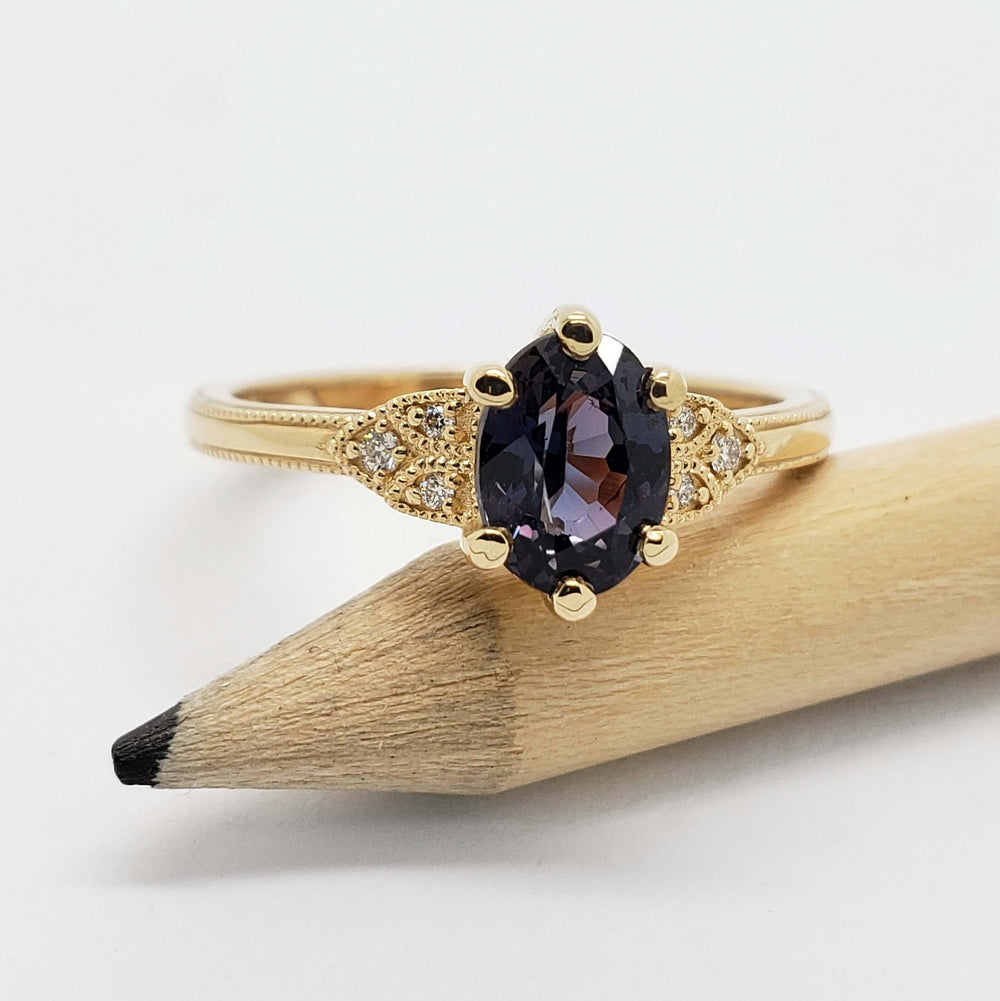 14kt yellow gold ring with oval purple sapphire and diamond details, displayed on pencil
